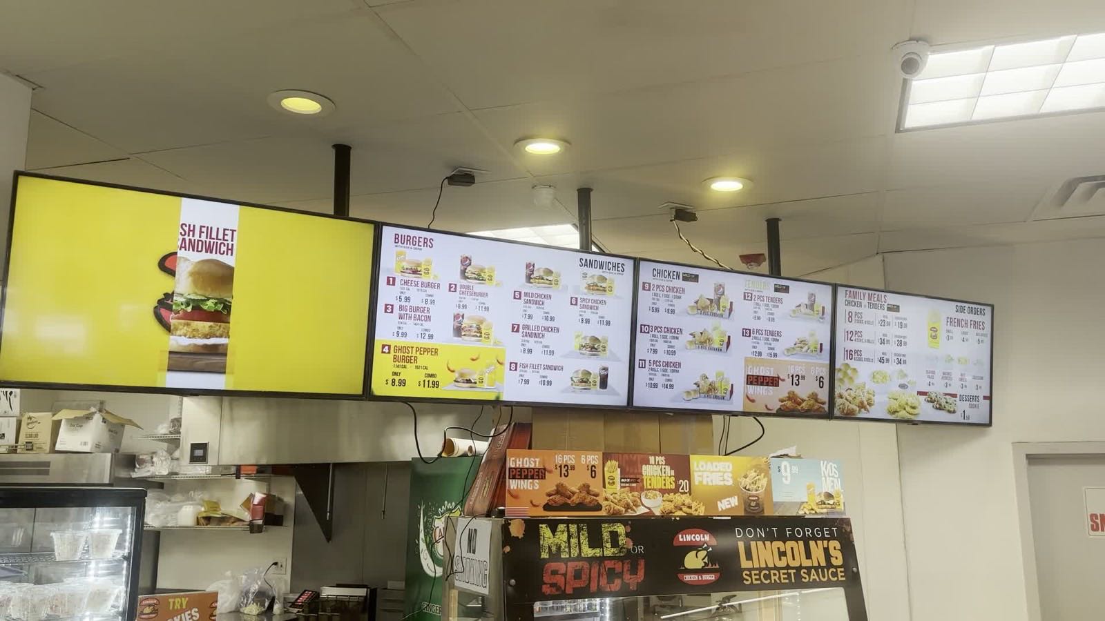 Row of four digital menu boards running live above a quick-service restaurant counter